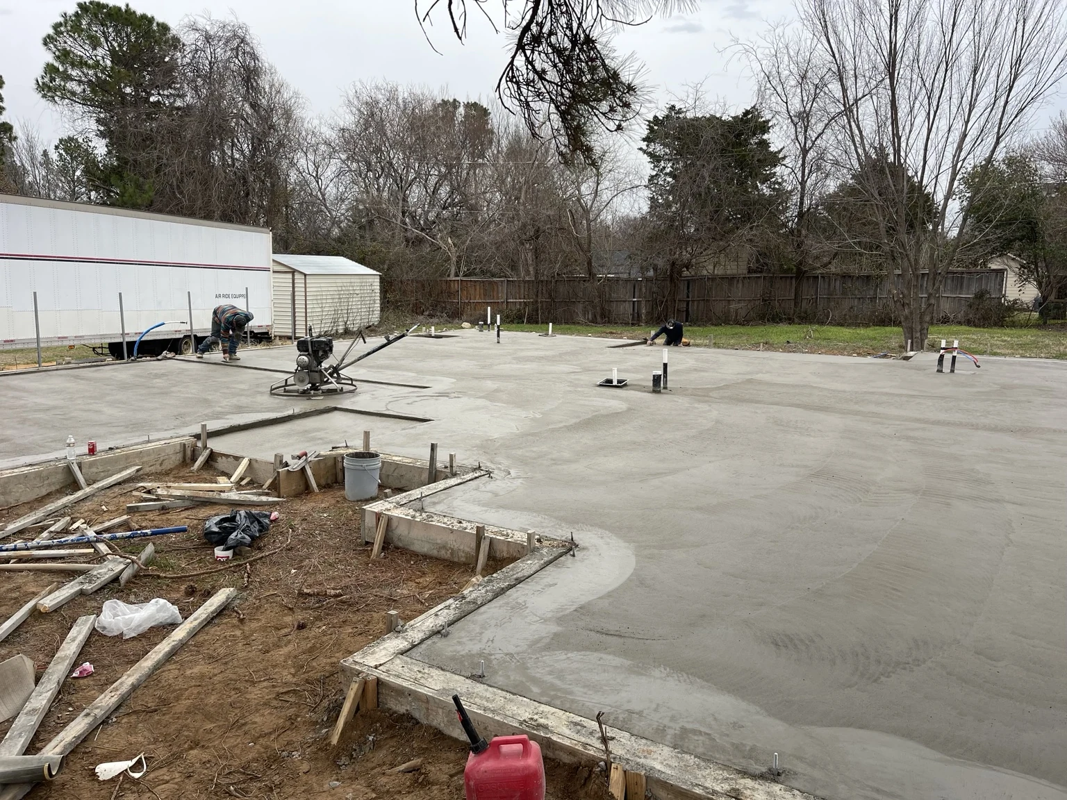 Workers finishing a newly poured slab with forms and service penetrations